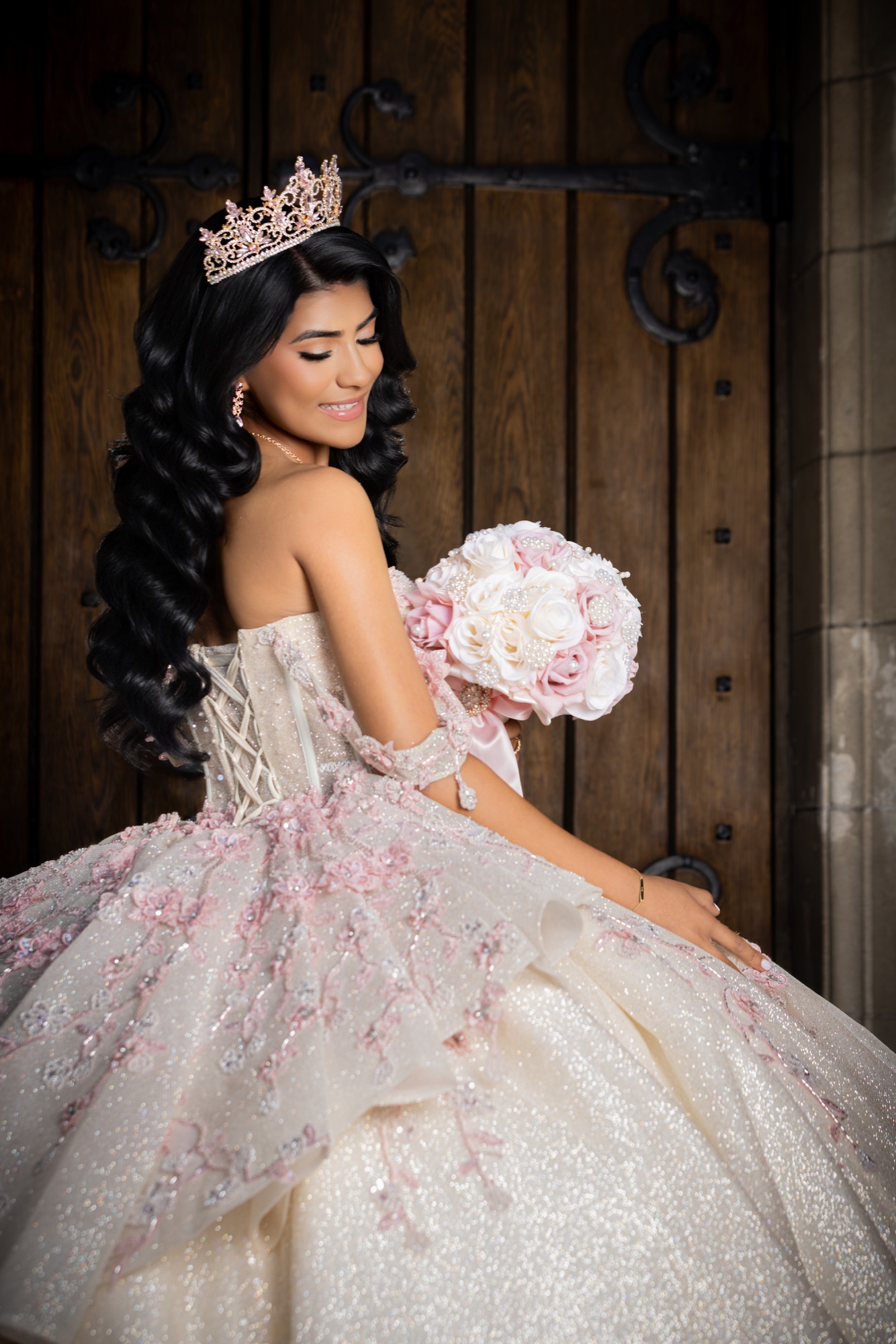 Quinceañera holding a pink and ivory bouquet against dark wooden doors