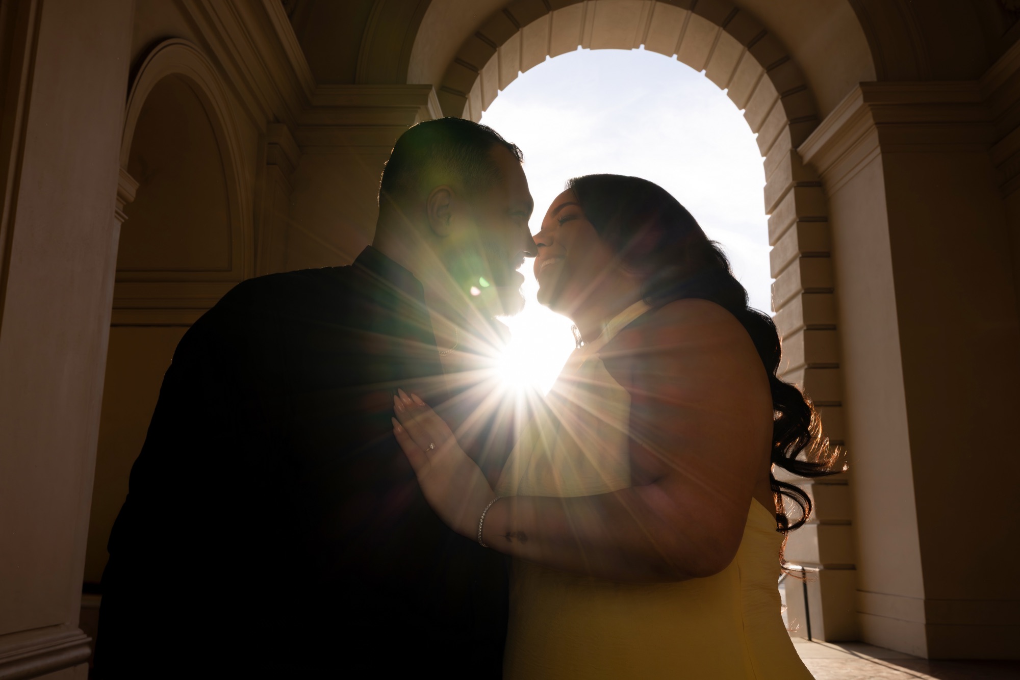 Couple leaning toward each other beneath an arch with sunlight between them