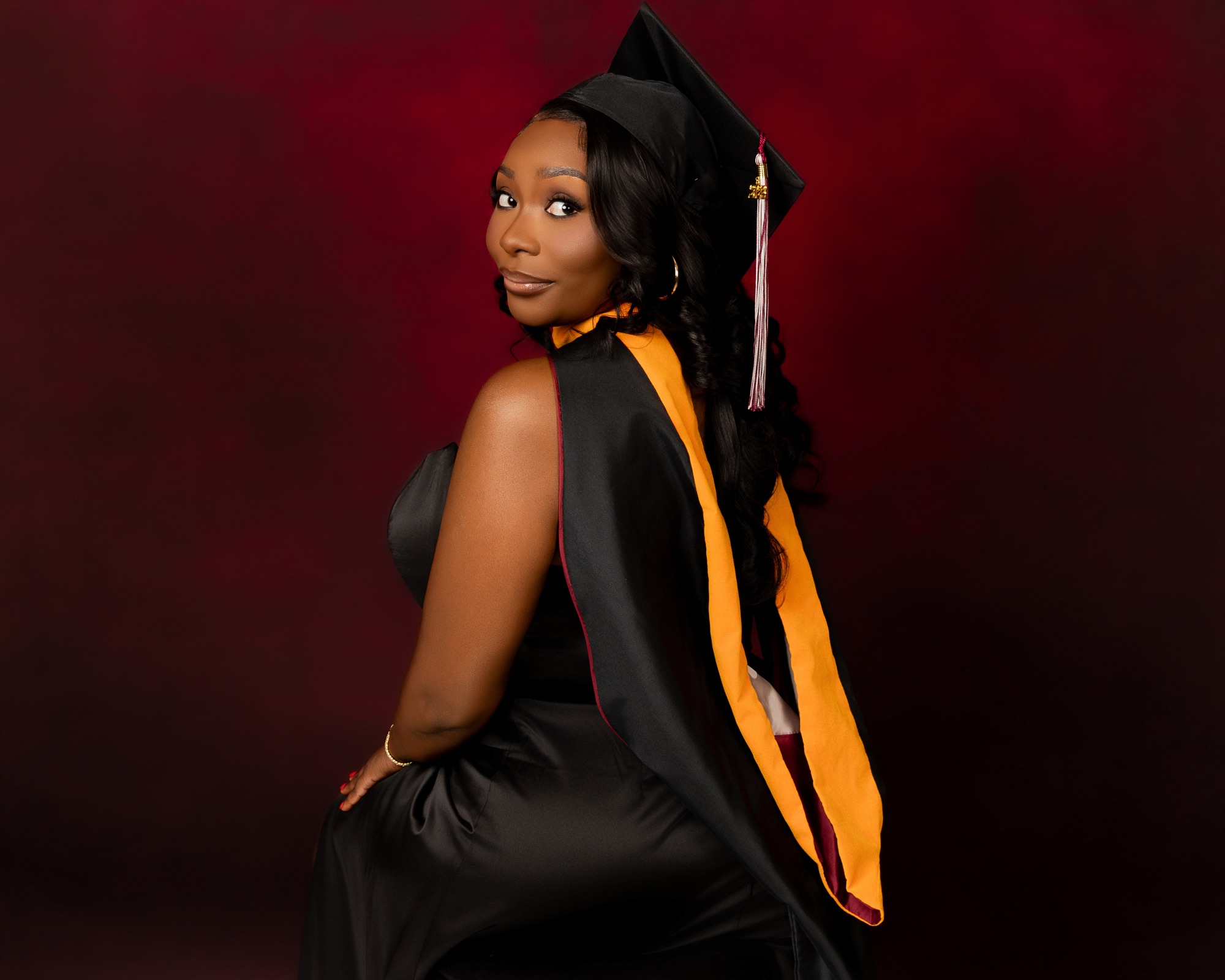 Graduate in a black cap and gown against a deep red backdrop