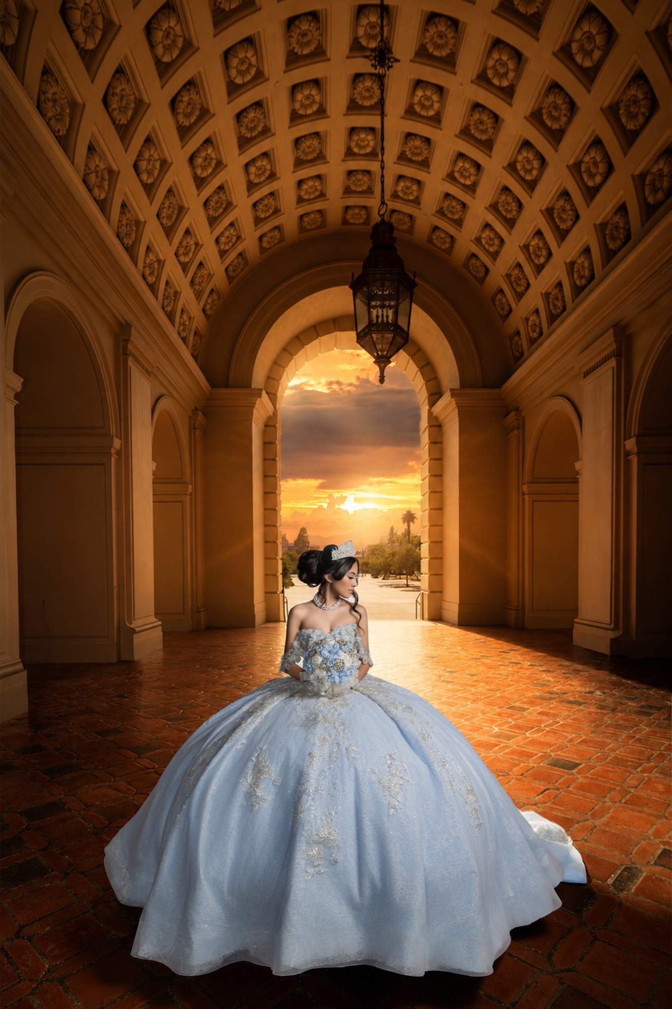 Quinceañera in a blue gown framed by a grand arch at sunset
