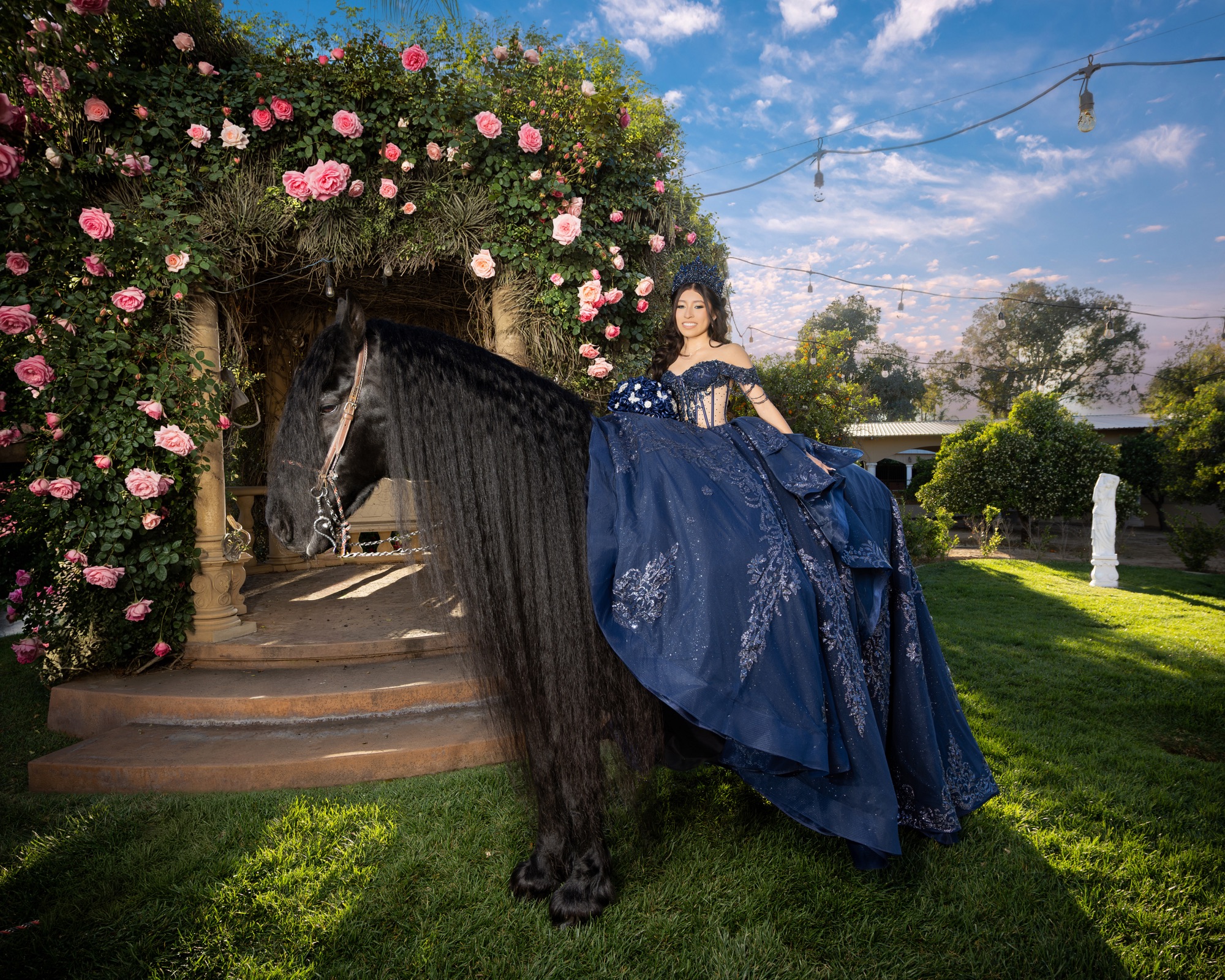 Quinceañera on a black horse beside a rose-covered garden pavilion