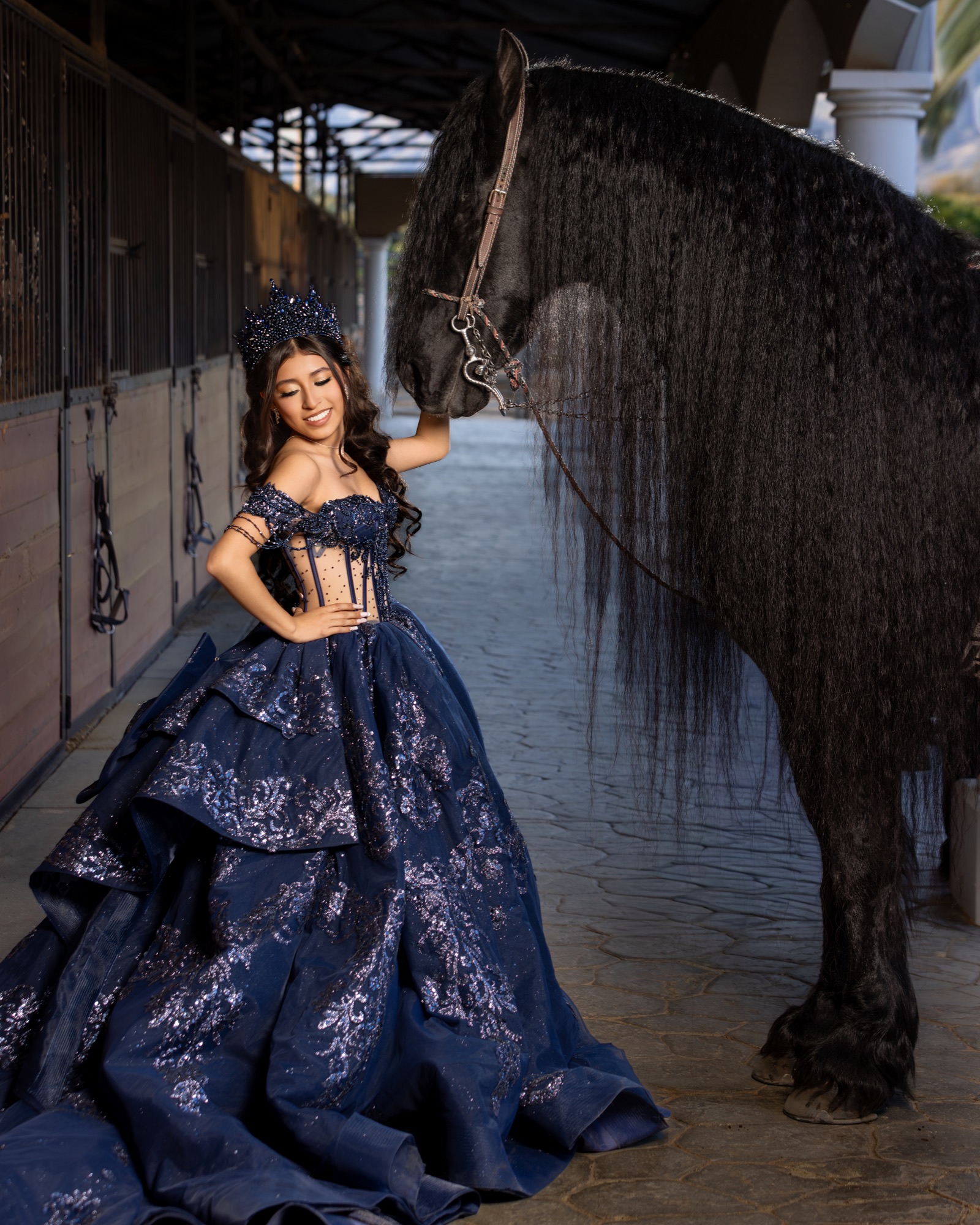 Quinceañera in a navy gown posing beside a black horse