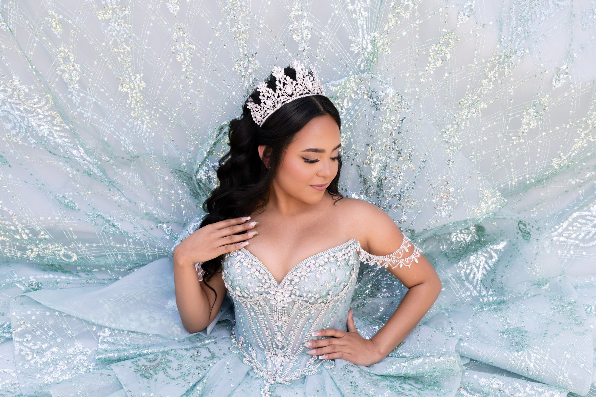 Portrait of a quinceañera surrounded by mint-colored embroidered fabric