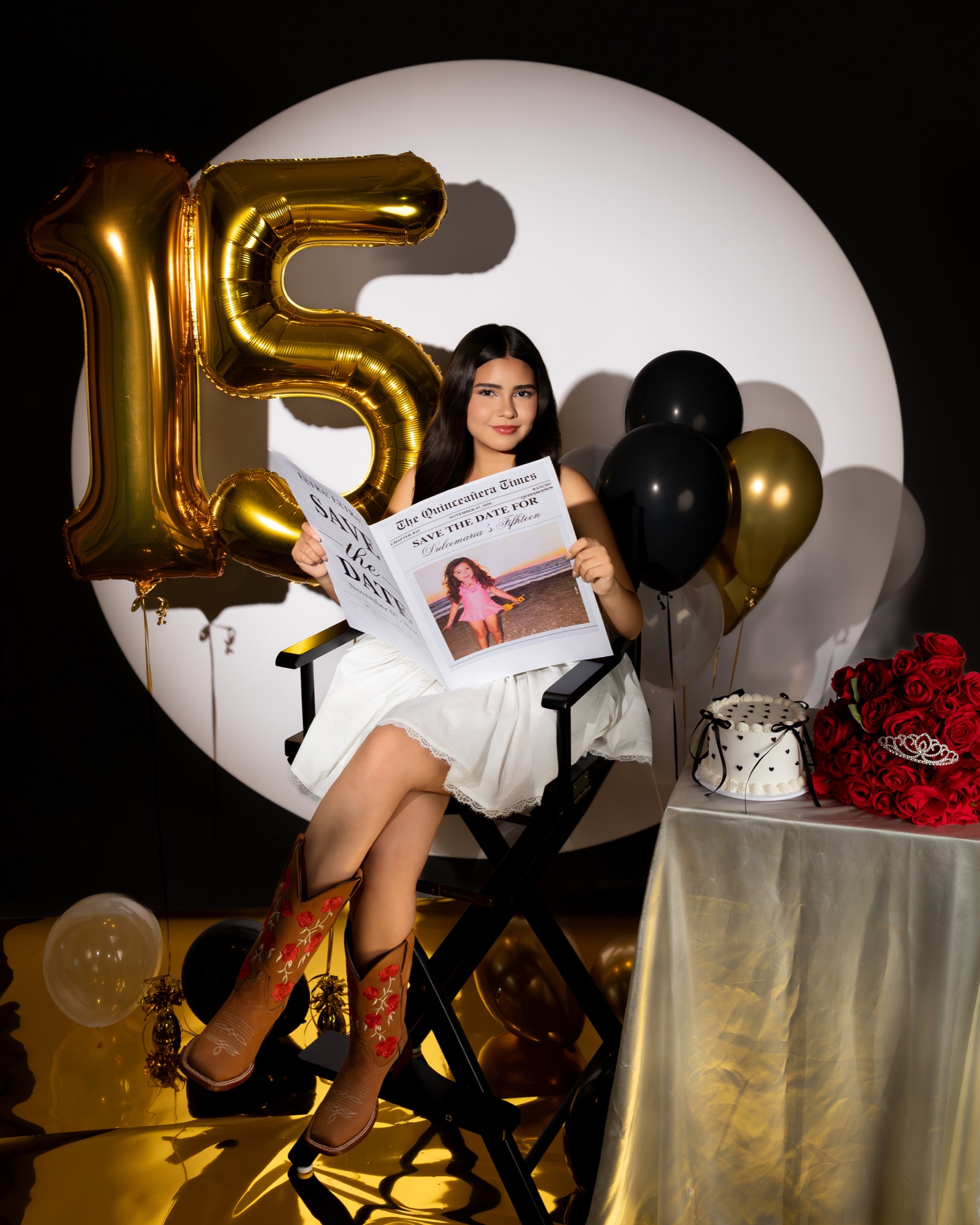 Quinceañera holding a save-the-date newspaper beside gold 15 balloons
