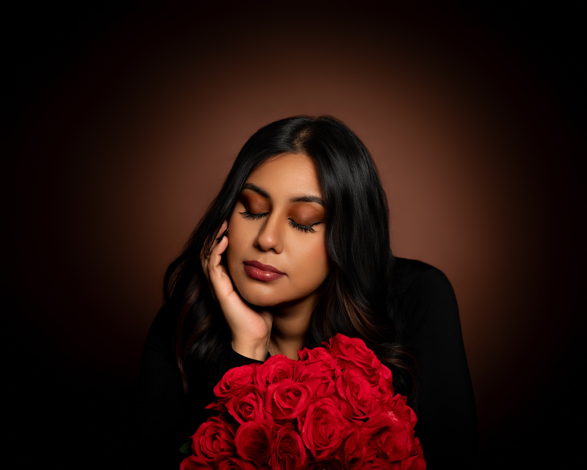 Studio portrait with red roses against a warm dark backdrop
